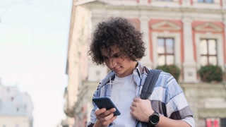 Blogger in headphones using smartphone, listening to music and browsing on smartphone. Outdoor, portrait. Man scrolls through social media on device, reading news on app