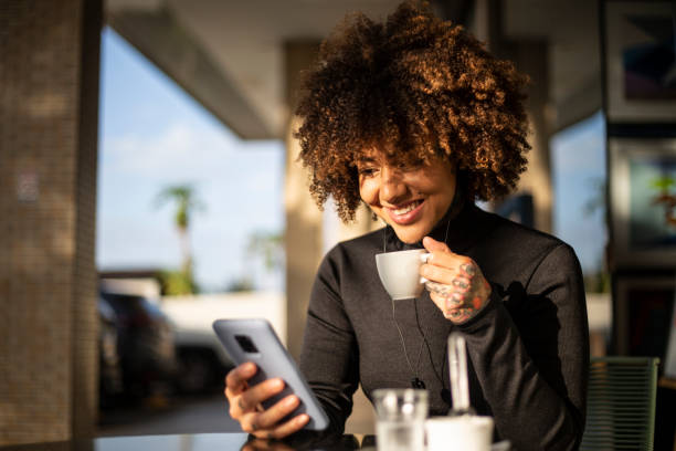 Black woman using cellphone and drinking coffee