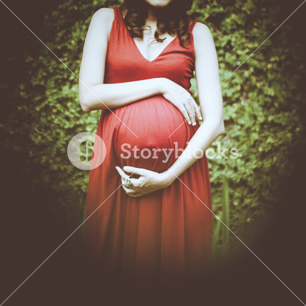 Image of pregnant woman touching her belly with hands relaxing outside in the park