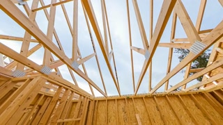 4k time lapse clip of wood roof beams of a new home construction site under blue sky and clouds passing by