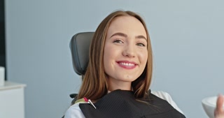 Satisfied Young Woman Giving Thumbs Up to Her Snow-White Smile in Dental Office